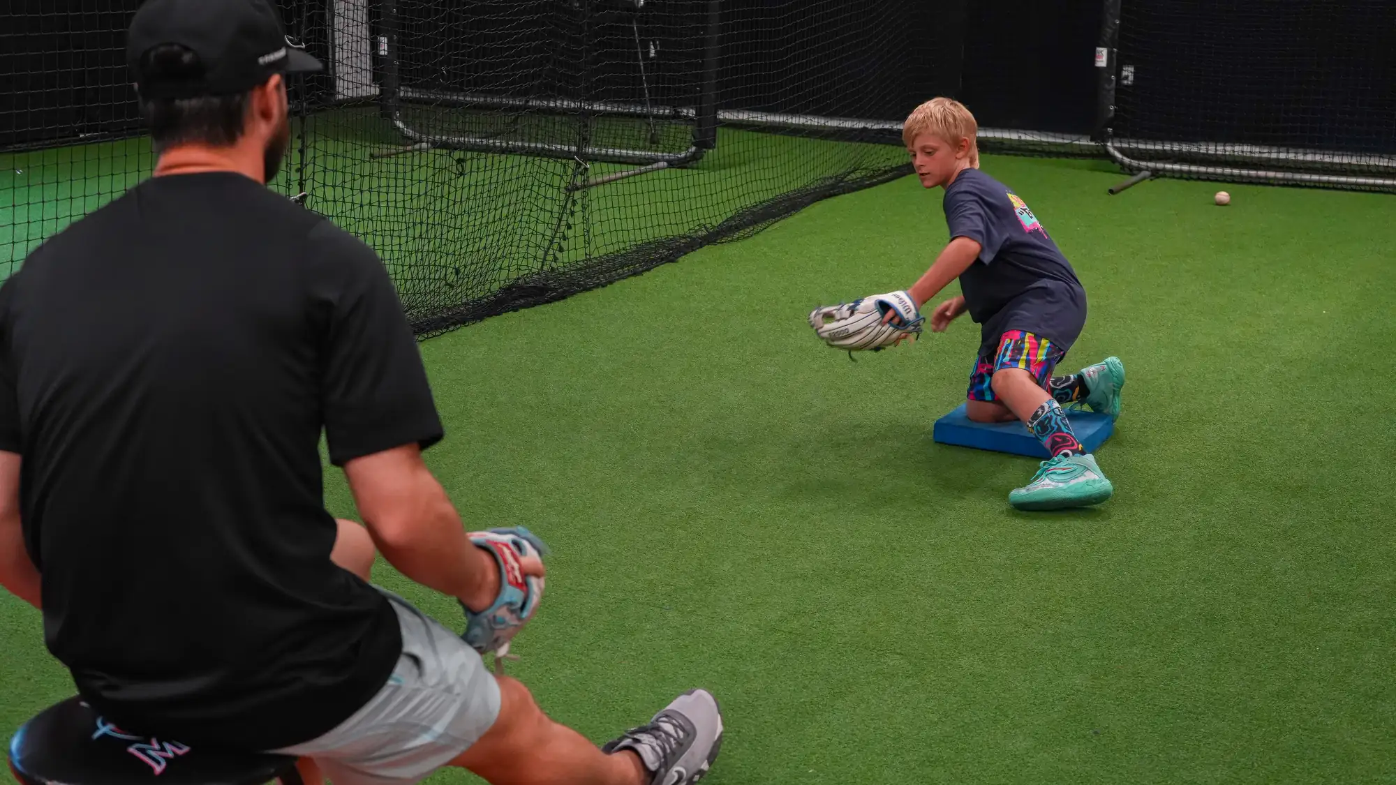XLB Training coach running ground ball reps with a youth infielder on the indoor turf