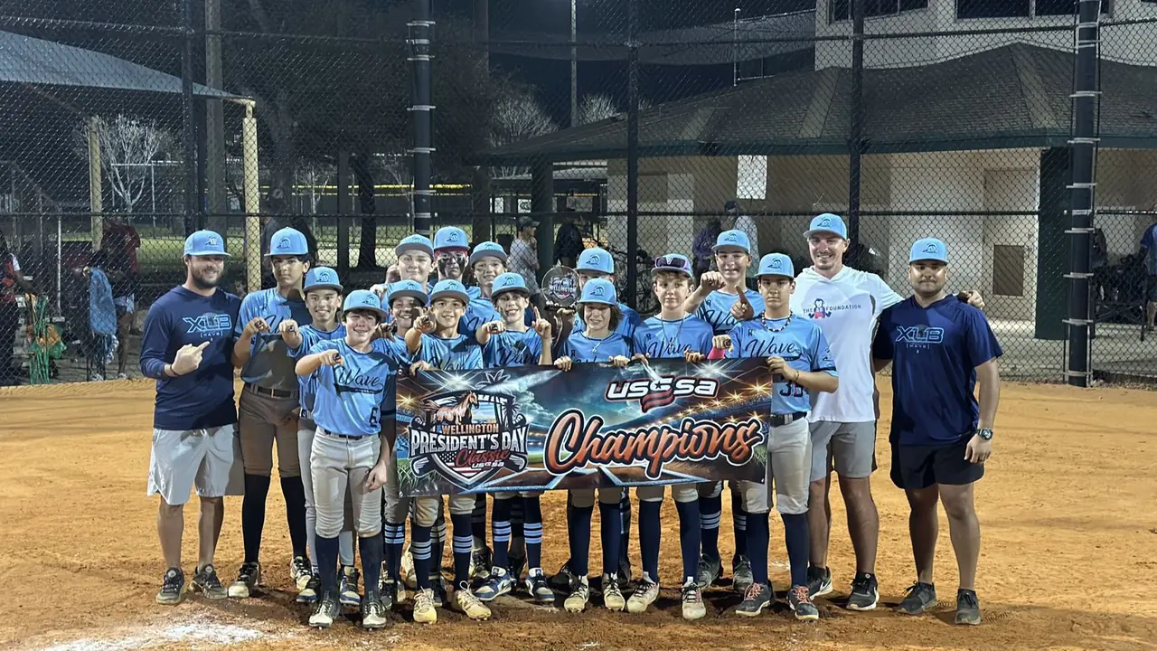 An XLB Wave youth travel baseball team and its coaches holding a tournament champions banner in Palm Beach County, Florida