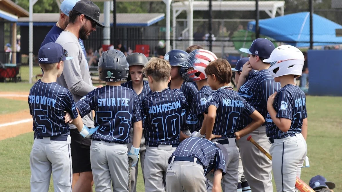 An XLB Wave coach leading a team huddle with youth travel baseball players in Boynton Beach, Florida