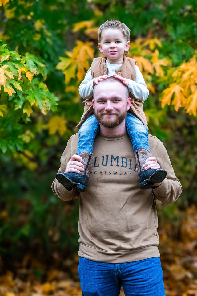 Father carrying his toddler on his shoulders in the autumn woods