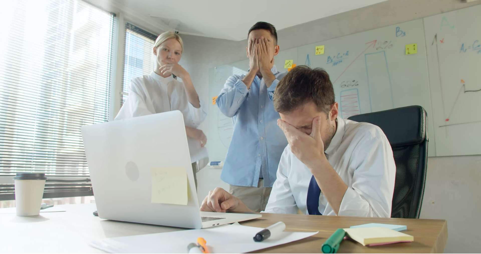 A team of three colleagues reacting to bad news on a laptop screen.