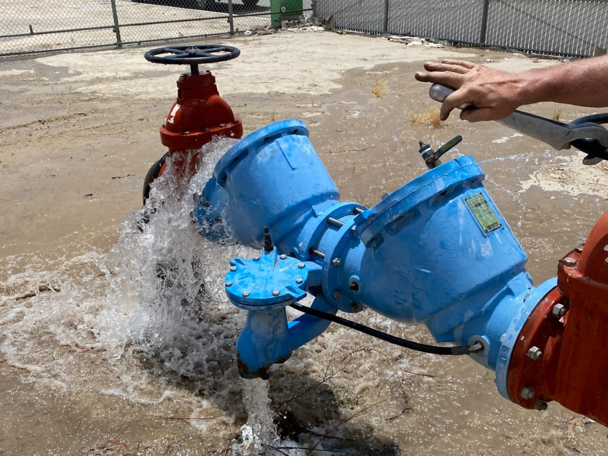 A blue backflow prevention device with red valves under pressure testing, where water is being released, showcasing a field test ensuring the device works correctly.