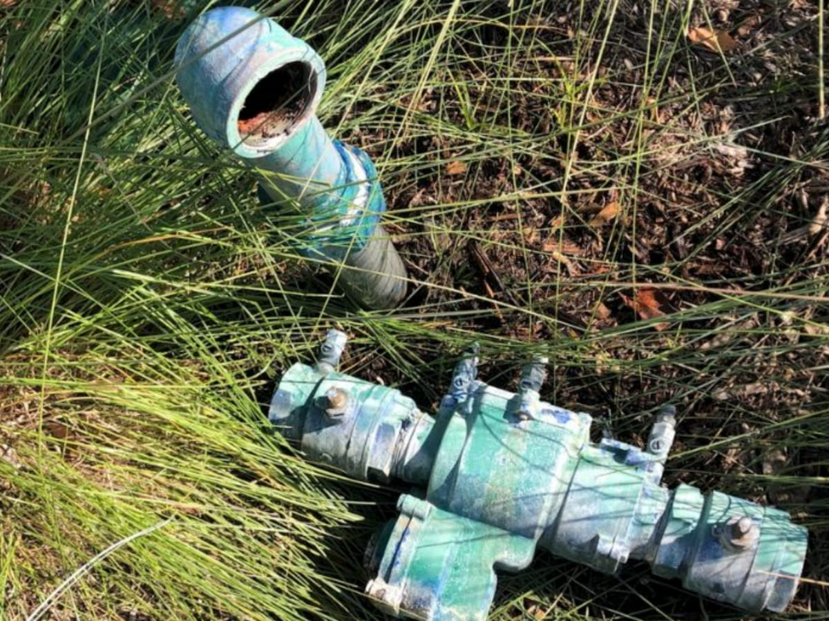 Corroded backflow prevention device lying near an outdoor pipe, showing the need for maintenance and water system protection.