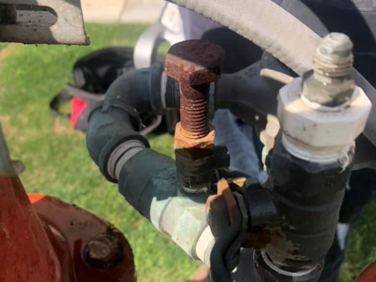 Close-up of rusted bolt on a backflow prevention device during repair, highlighting maintenance needs for water safety.