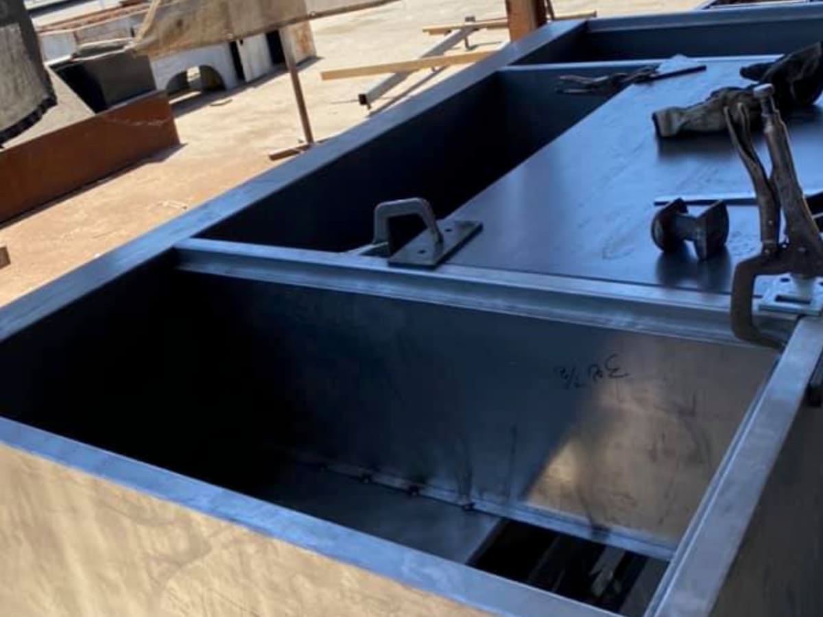 A large metal industrial box being fabricated in a workshop, likely part of a water system or backflow device, representing heavy-duty components used in backflow prevention installations.