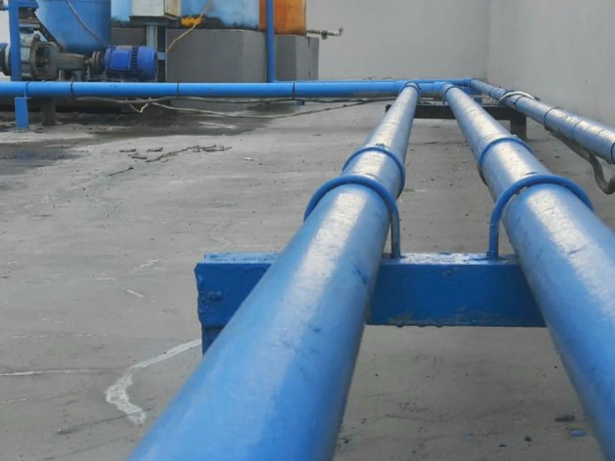 Blue pipes running horizontally across a building’s roof in an industrial setup, demonstrating a section of a larger water system involved in preventing contamination through backflow.