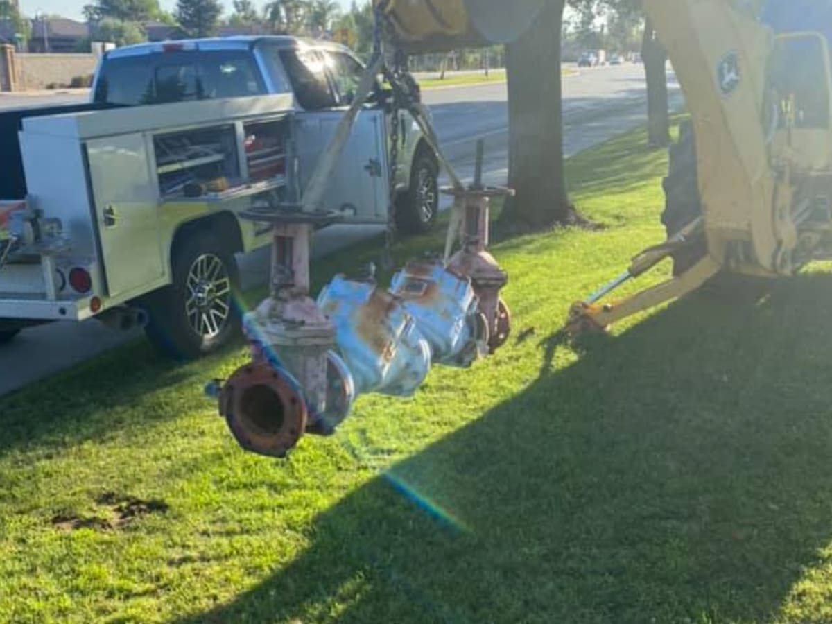 A backflow prevention device being removed by a crane during a repair or replacement process, illustrating large-scale maintenance on water systems.