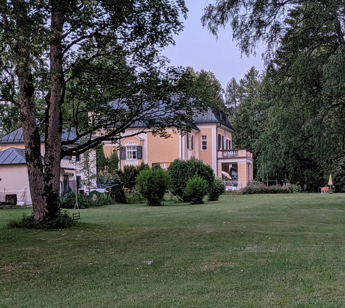 The house across the lawn at dusk, windows lit