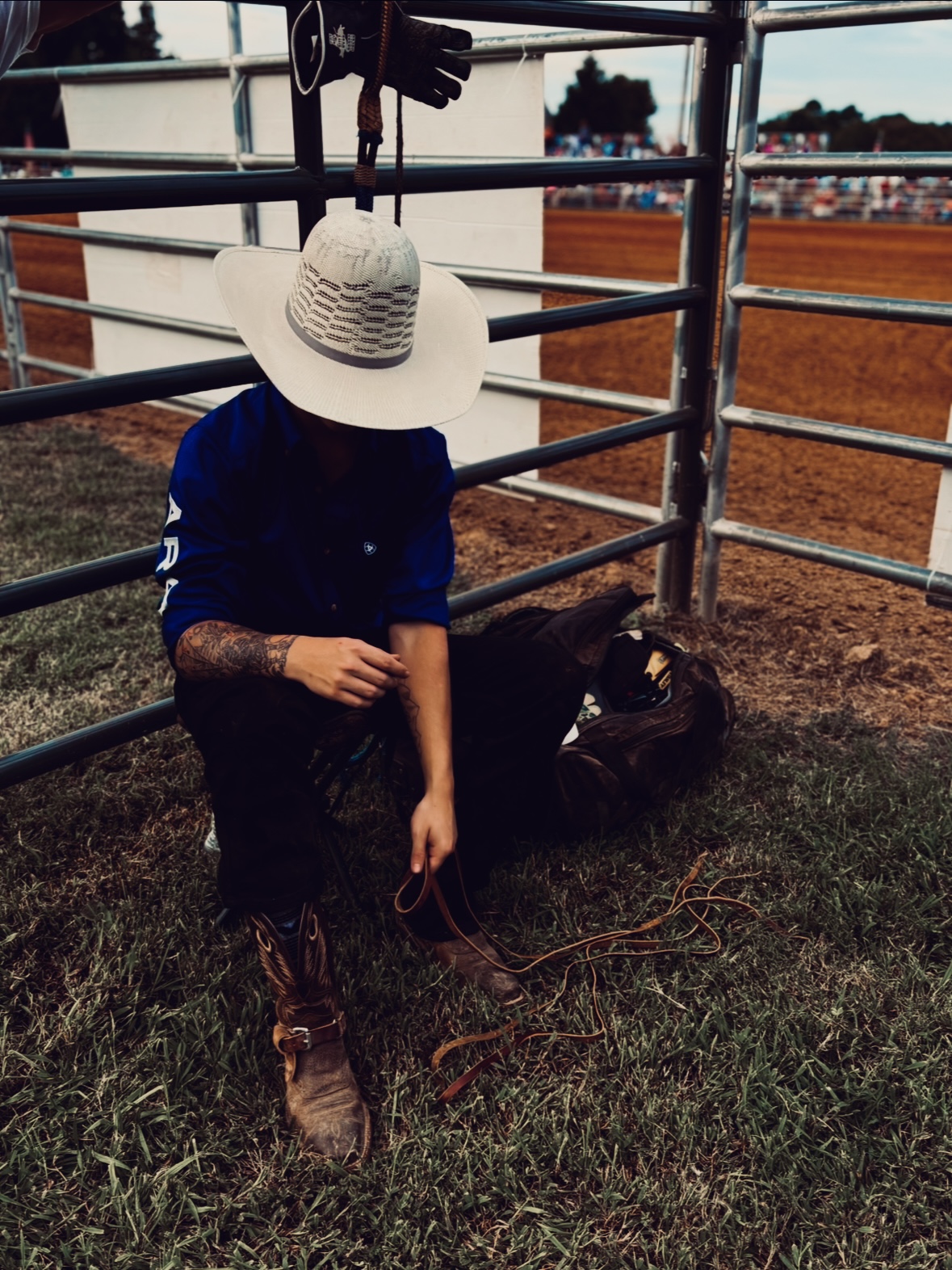 Greylen Simmons at a rodeo, wearing a straw cowboy hat, gearing up behind the chutes
