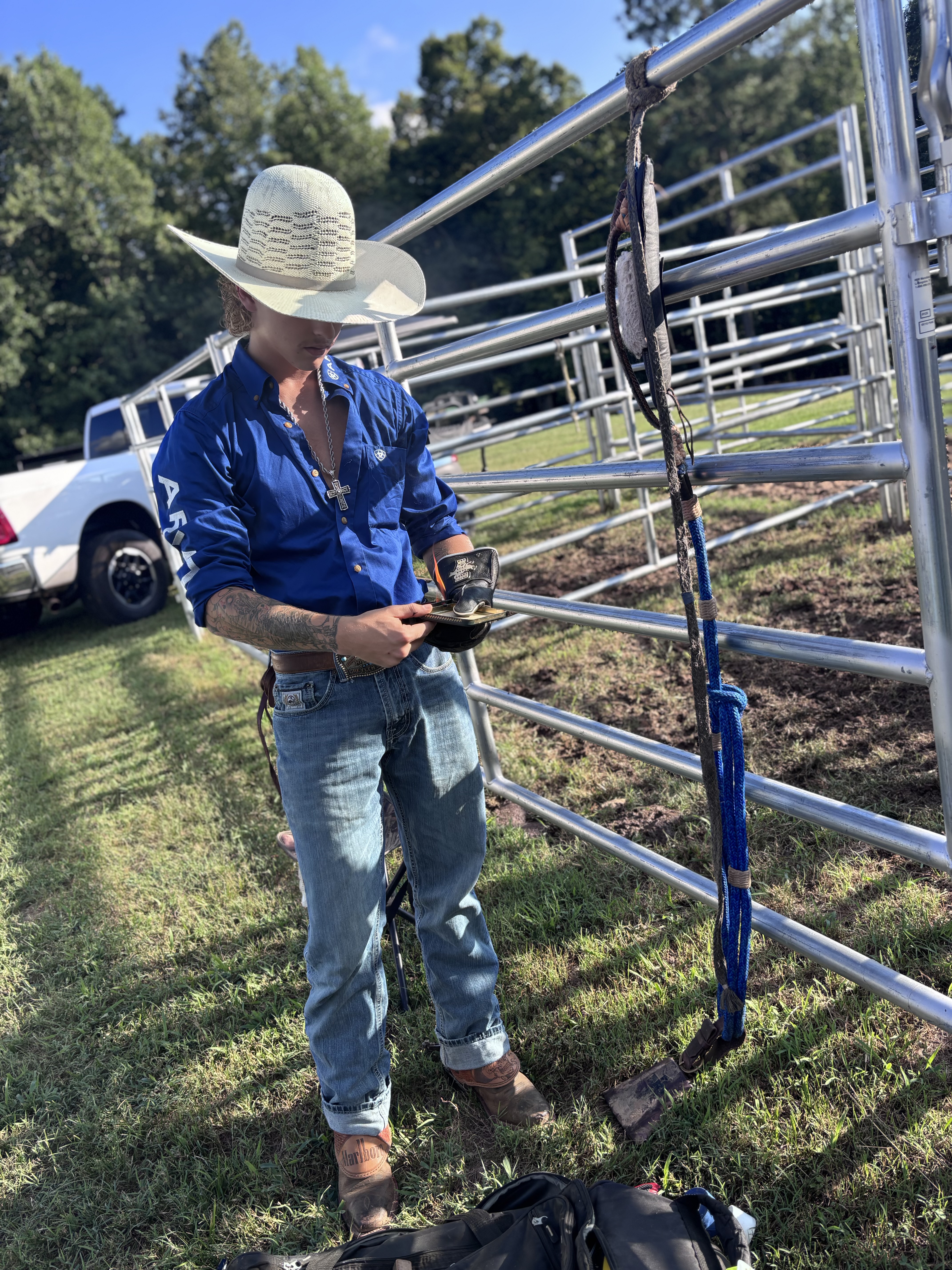 Greylen Simmons at a rodeo, wearing a straw cowboy hat beside the arena gates