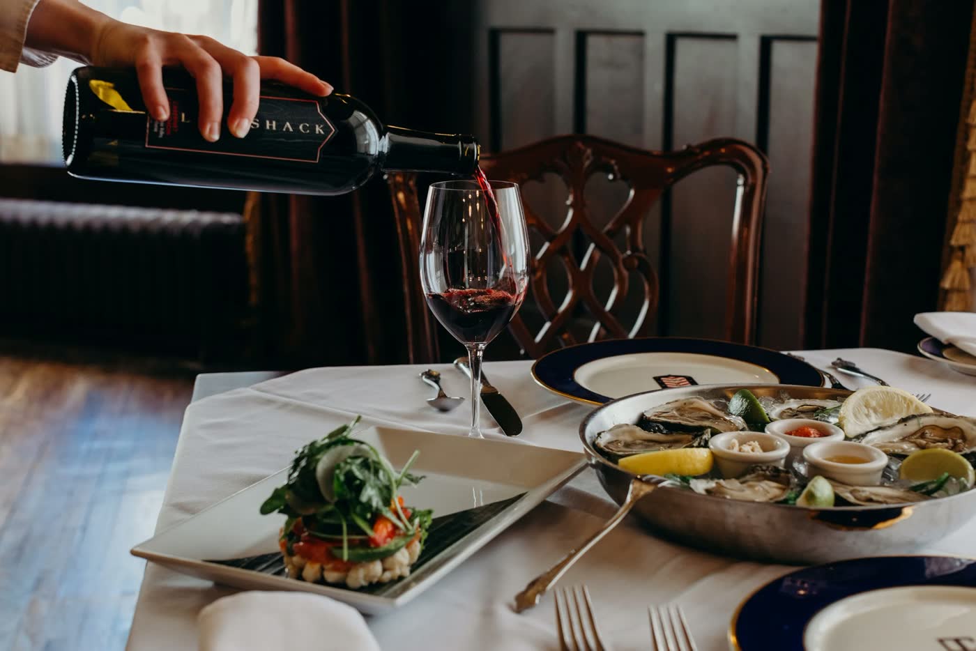 Wine poured at a white-linen table set with oysters in Bohemia