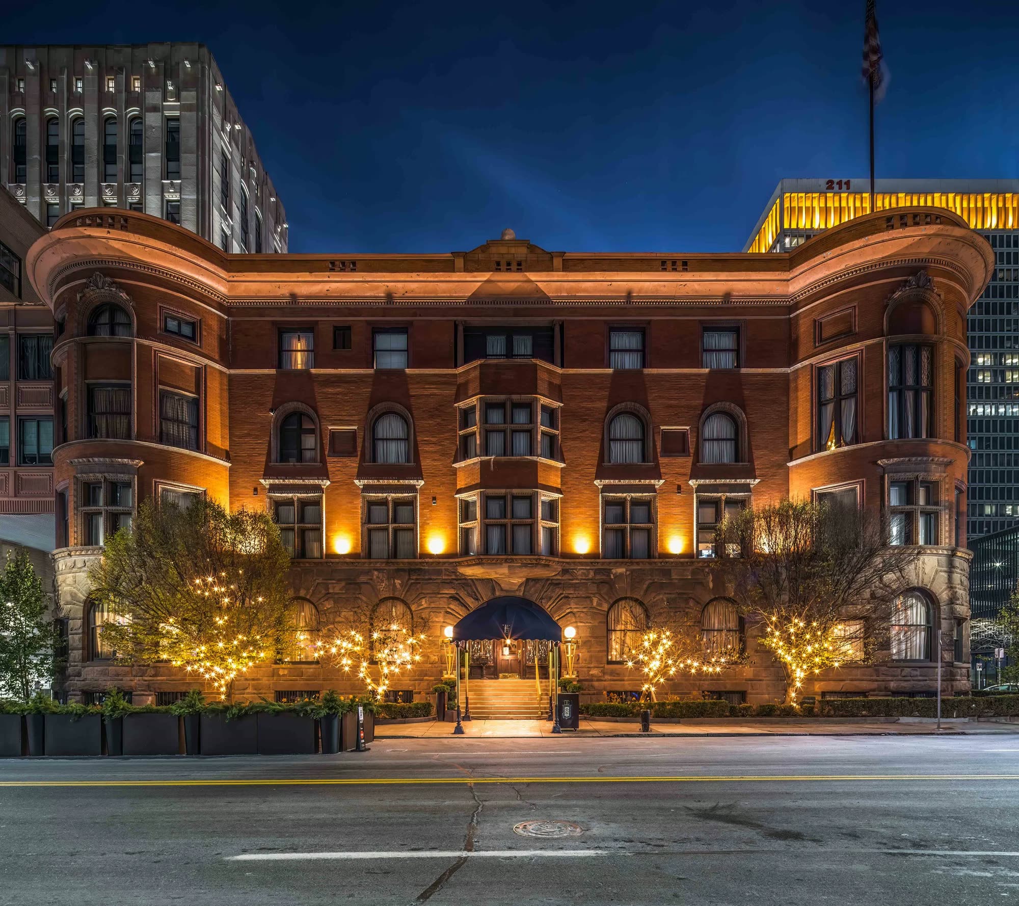 The Romanesque brick building at Fort and Cass lit warmly at night, its arched entrance glowing beneath string-lit trees