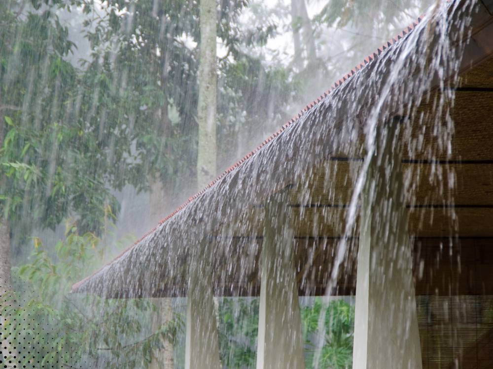 Close-up of rainwater flowing off the edge of a roof, highlighting water droplets in the midst of a storm, emphasizing  roof drainage during wet weather conditions