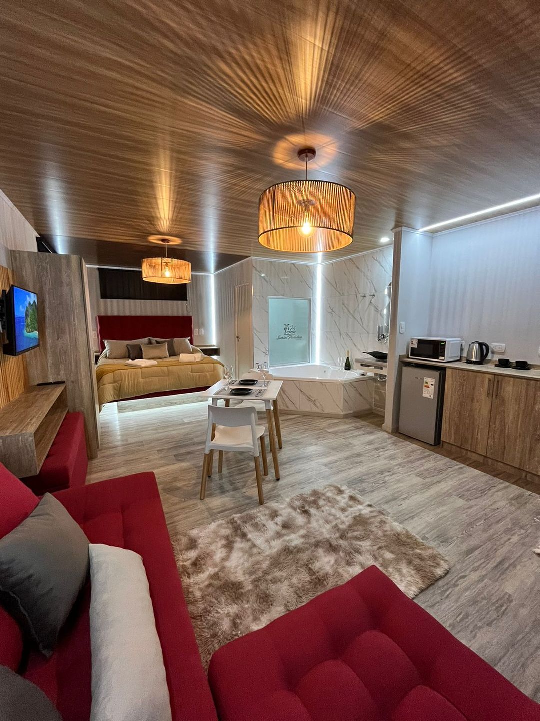 Vista general de la suite: cama King con respaldo de terciopelo, hidromasaje de mármol, living rojo y lámparas de ratán