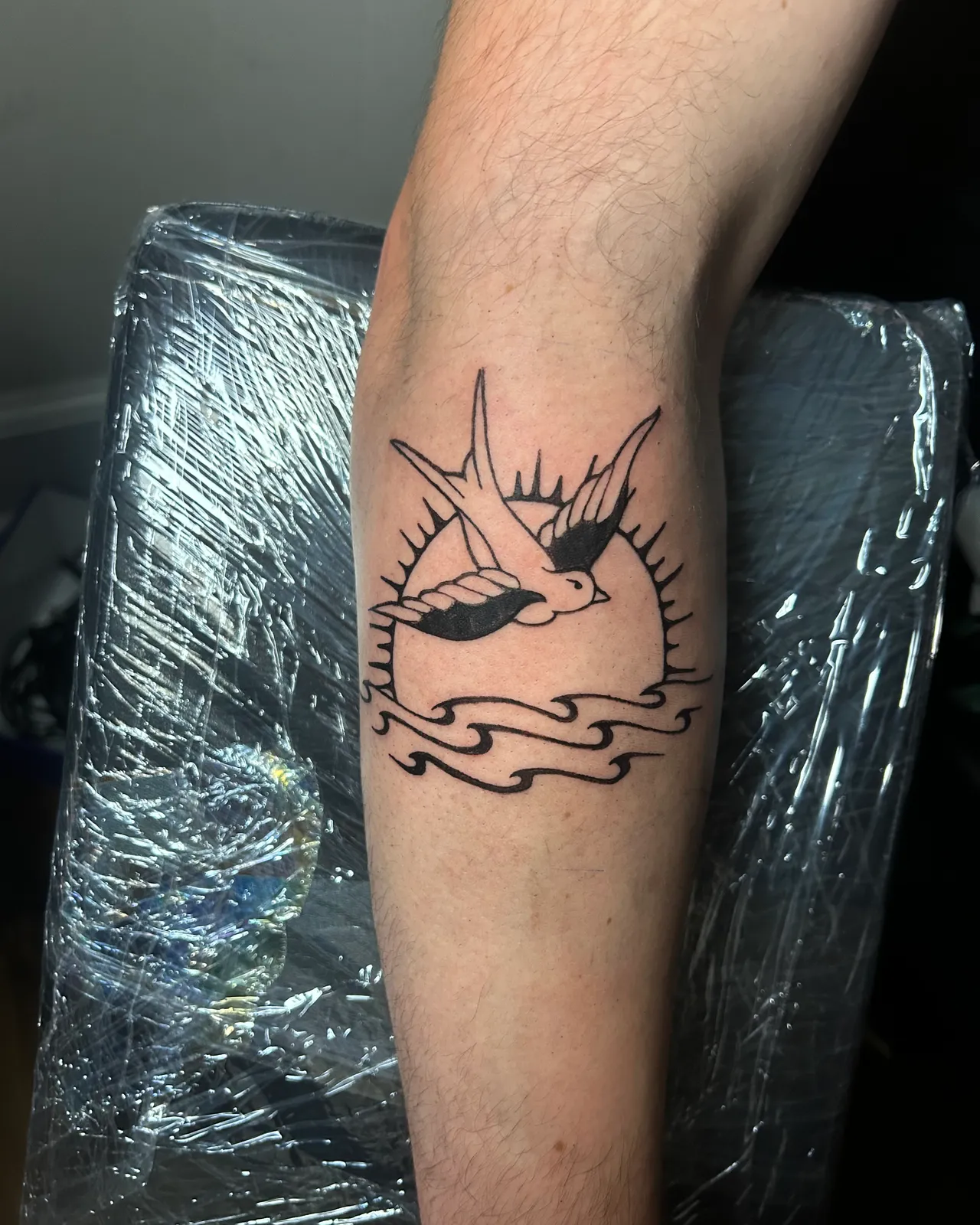 Traditional swallow over a rising sun and waves forearm tattoo by Slick at Studio AZ Tattoo Minneapolis