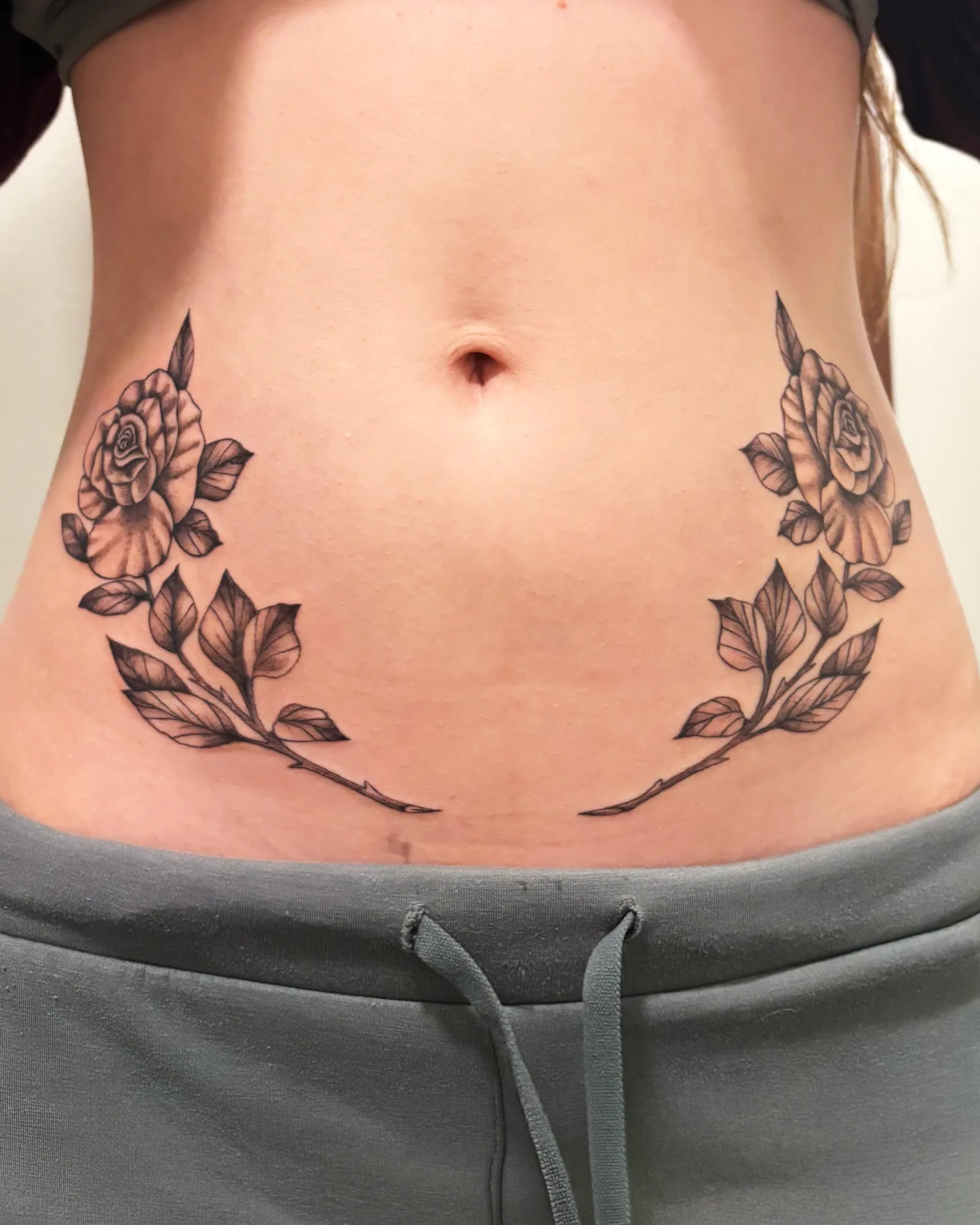 Black and grey symmetrical rose and leaves stomach tattoo by Meg at Studio AZ Tattoo Minneapolis