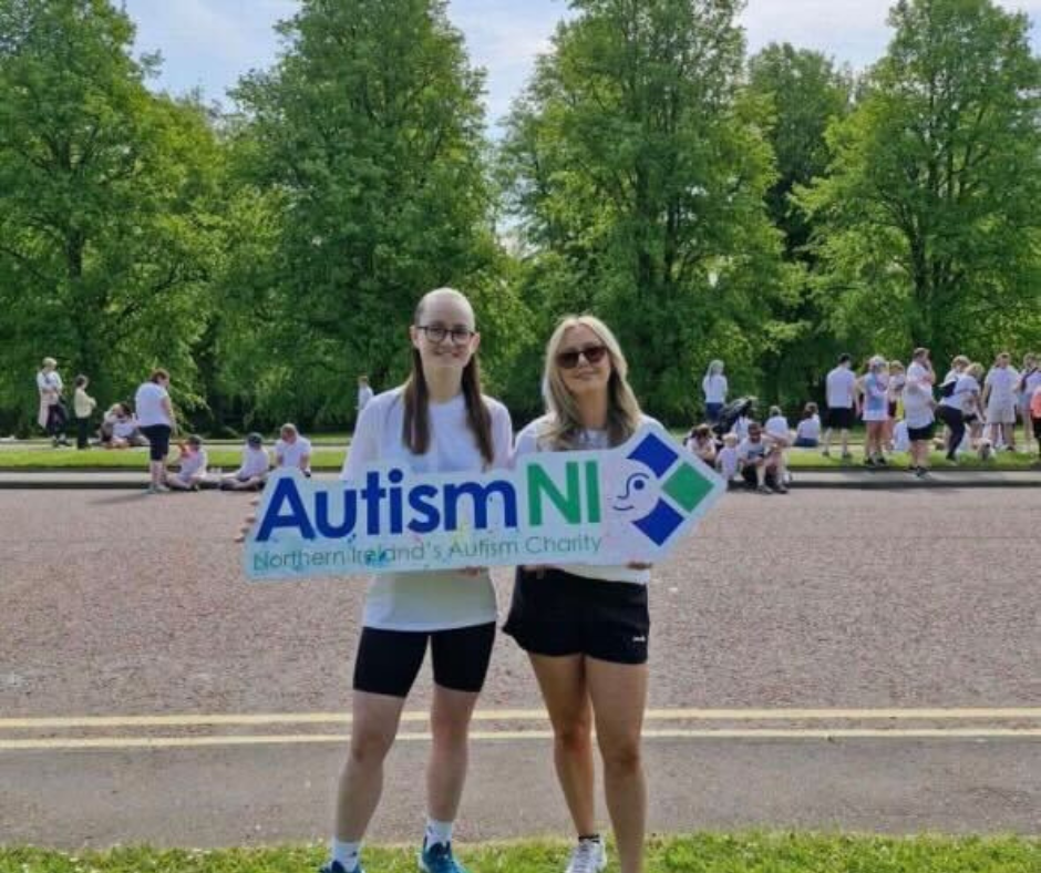 Two coaches holding the Autism NI charity sign at a fundraising event