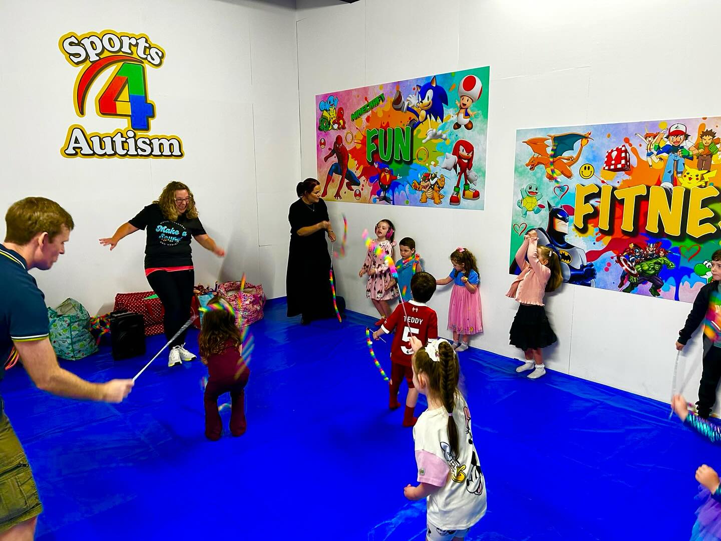 Children and coaches playing together with rainbow ribbons on the blue mat under the Sports 4 Autism logo