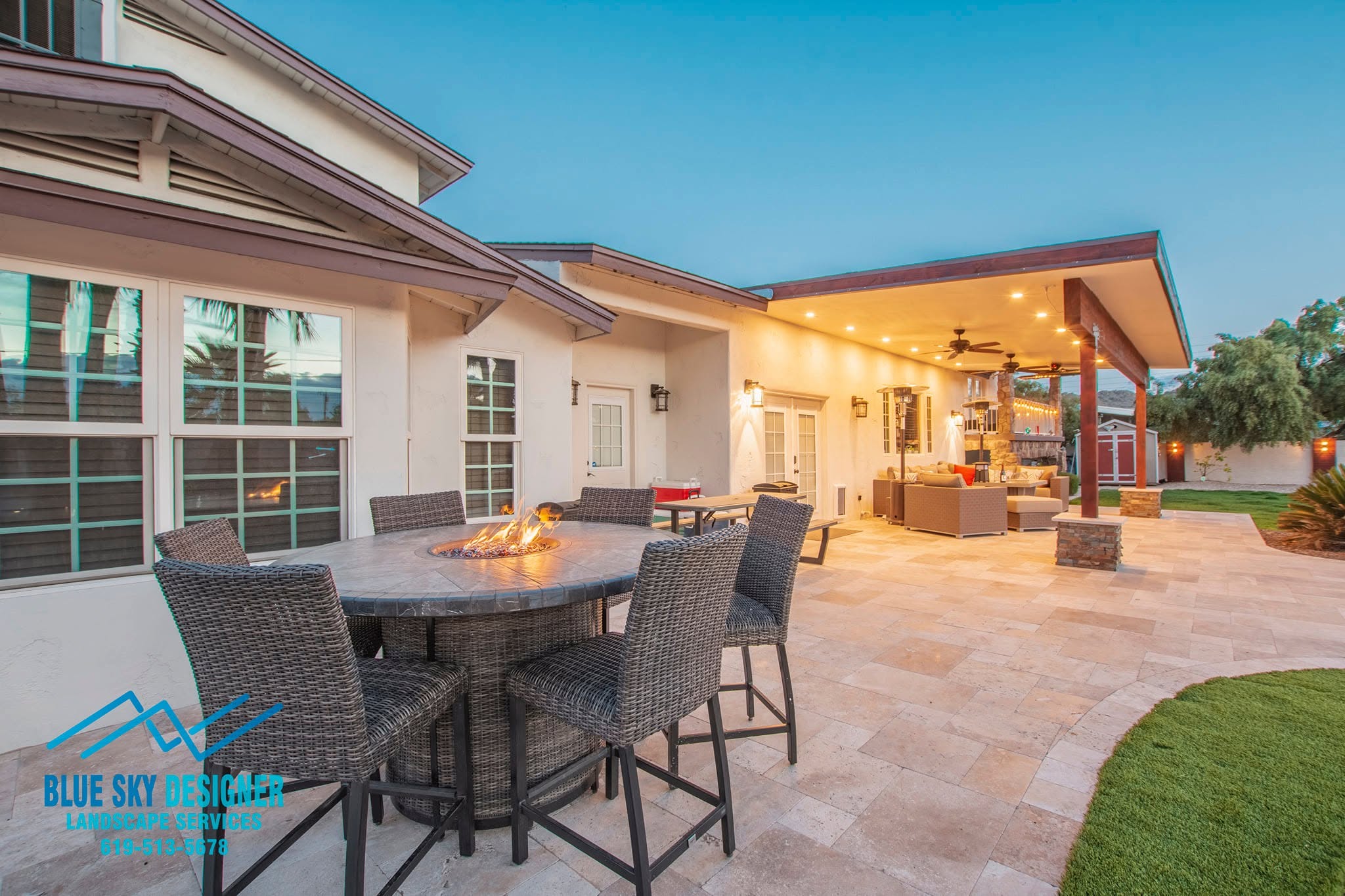 A finished paver patio installed by Blue Sky Designs in a Cave Creek backyard, with desert landscaping and natural stone surroundings visible. The hardscape surface extends from the home's back entrance toward an open outdoor seating area under the Arizona sky.
