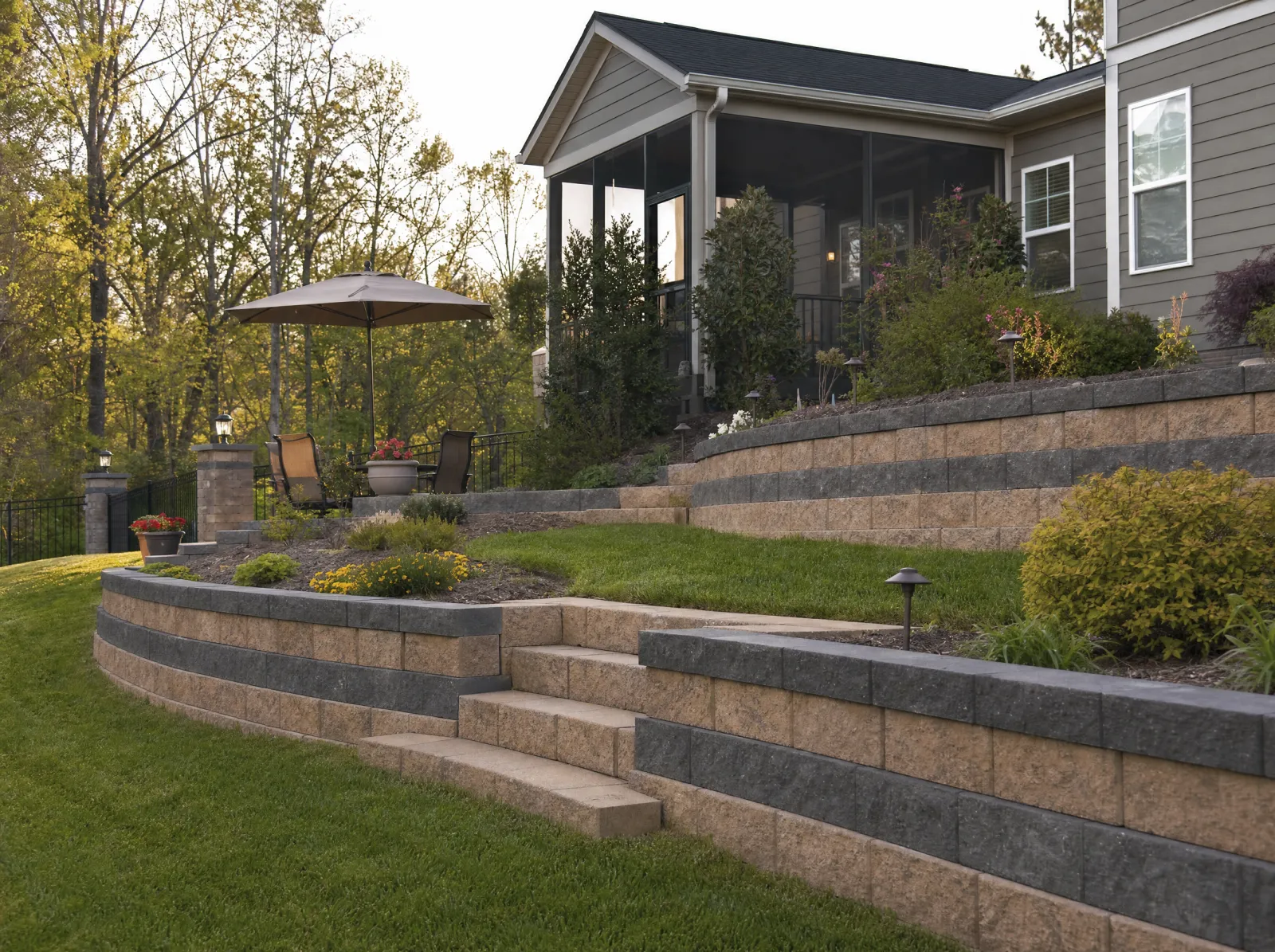 Design concept: Two-tier segmental block retaining wall in tan and charcoal with block steps between tiers, planted beds, suburban backyard.