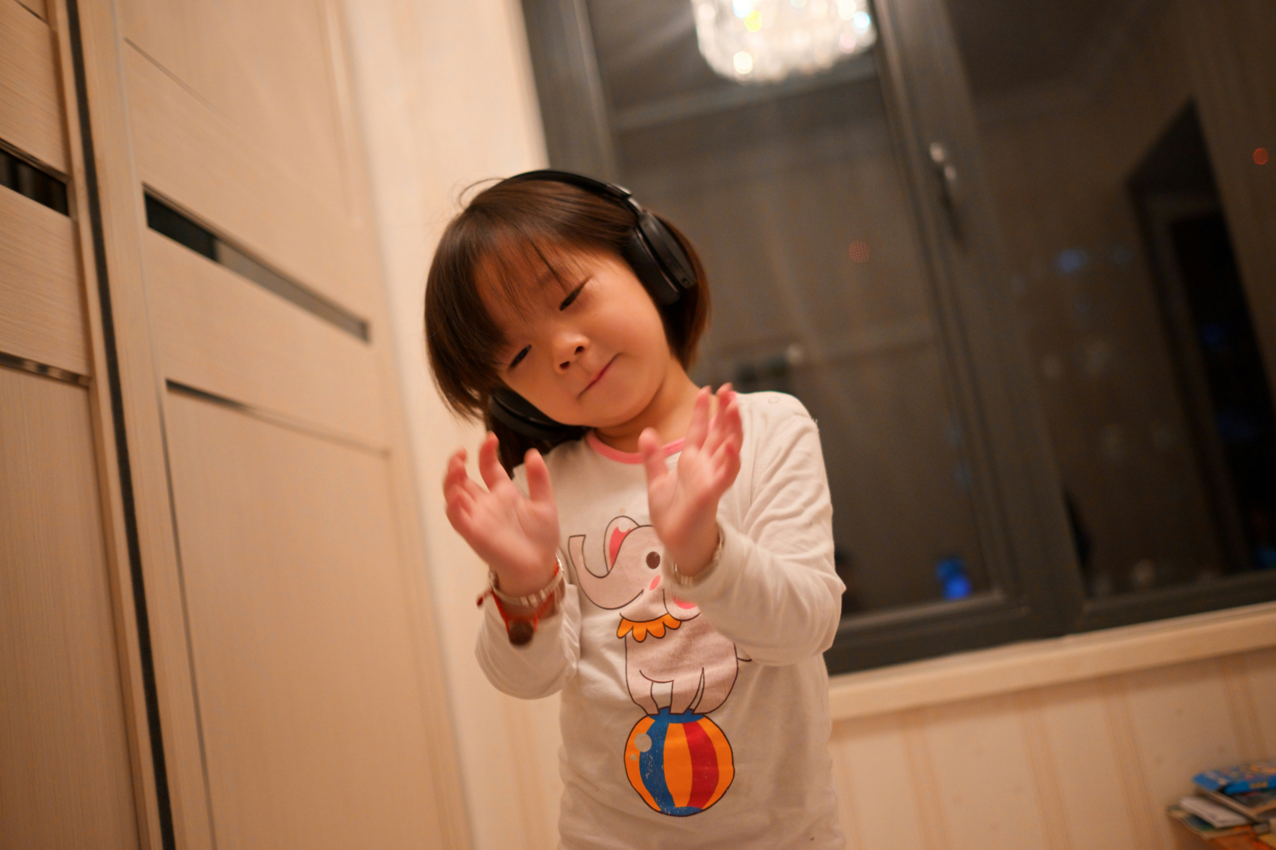  A young child clapping hands while listening to music through wireless headphones.