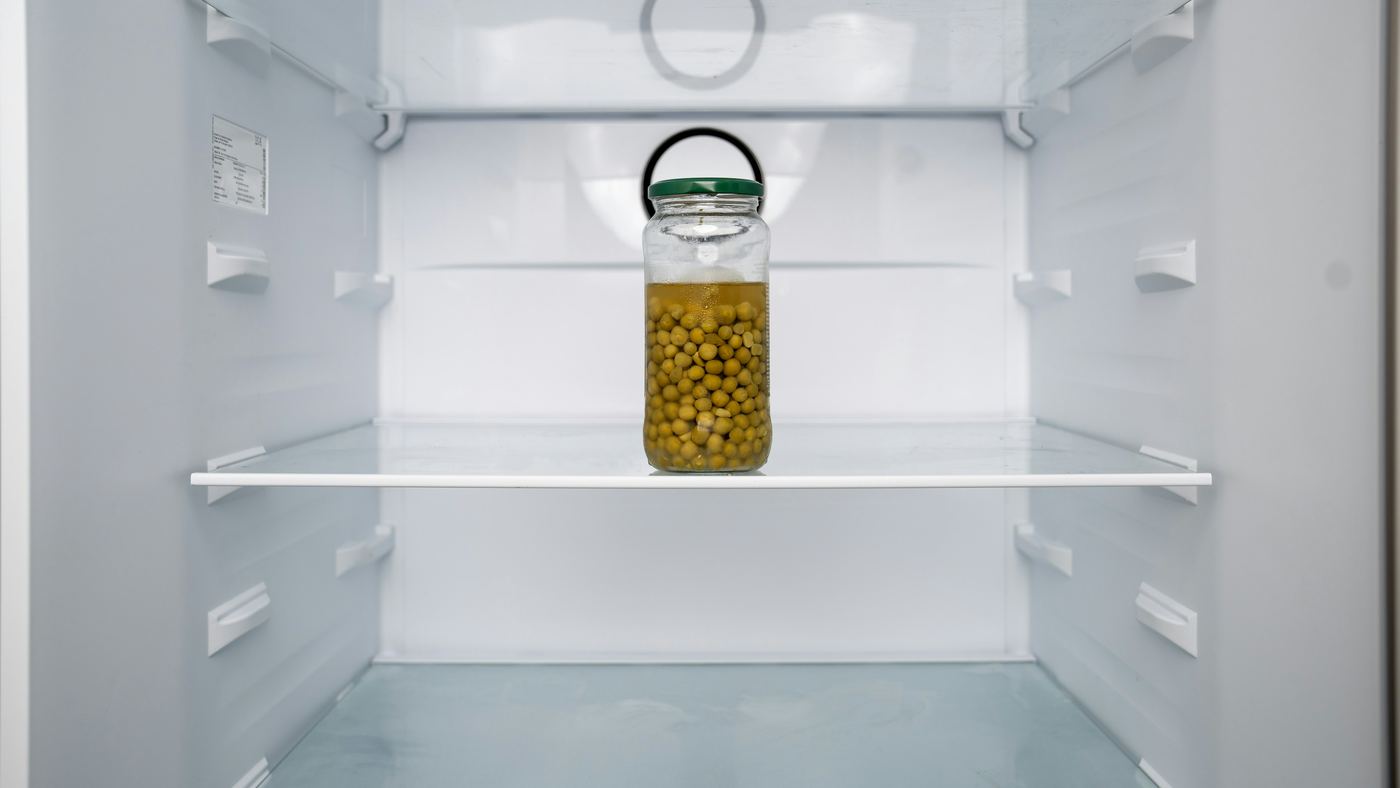 Open refrigerator with empty glass shelves and a single jar of peas
