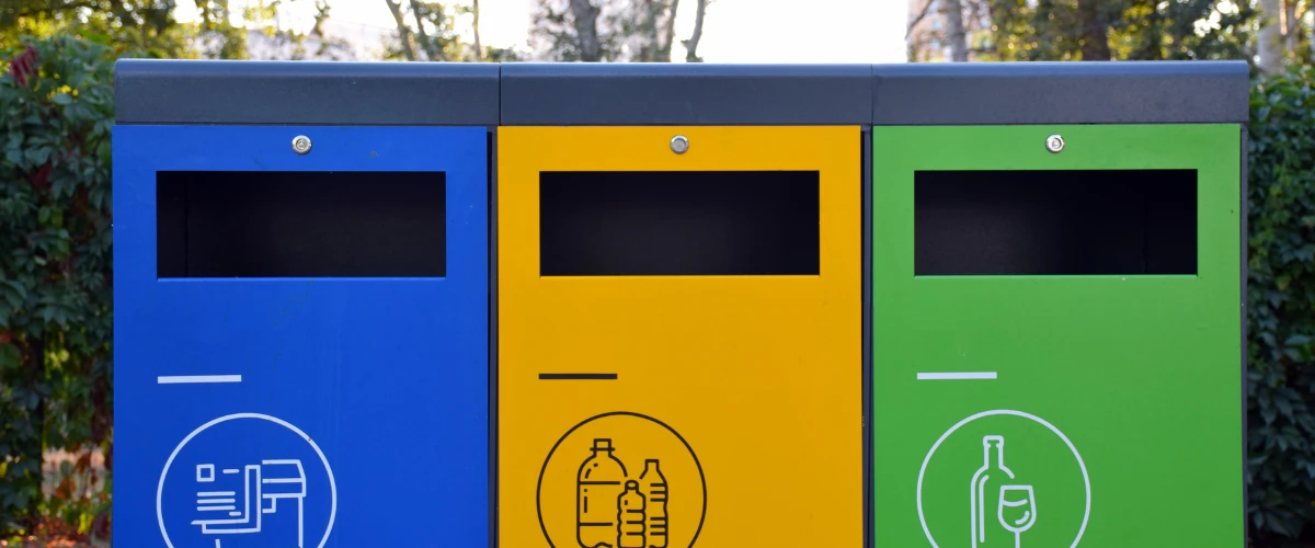 Recycling sorting station with blue, yellow, and green bins used for separating paper, plastic, and glass waste.