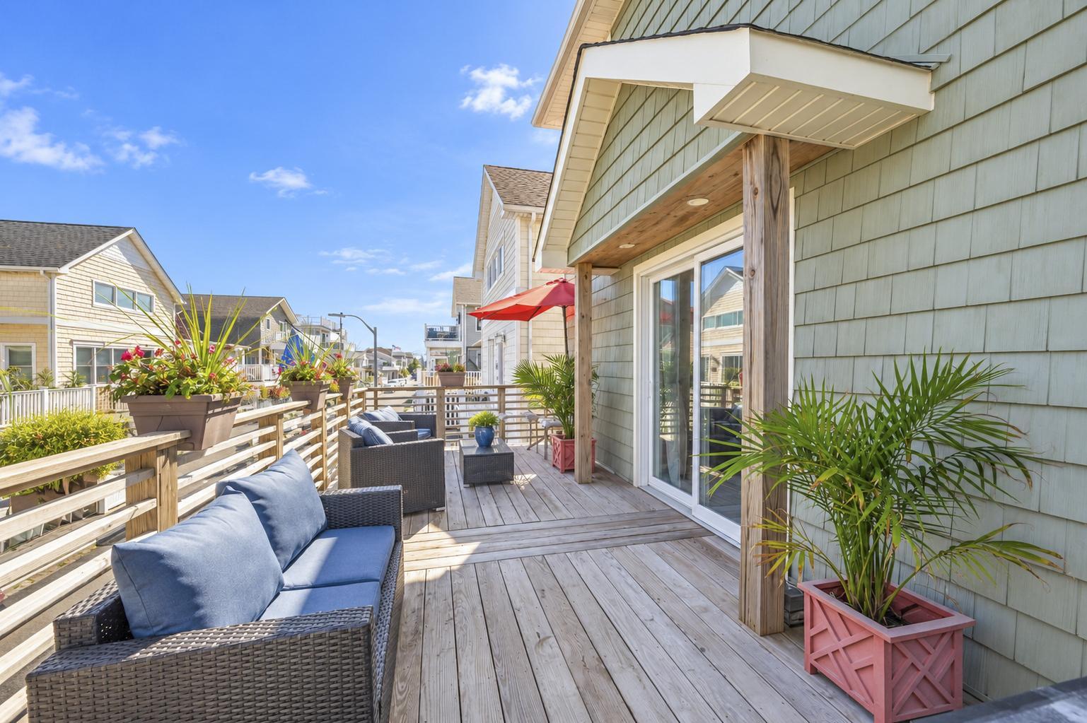 Sunny front deck with lounge seating, greenery, and sliding glass doors