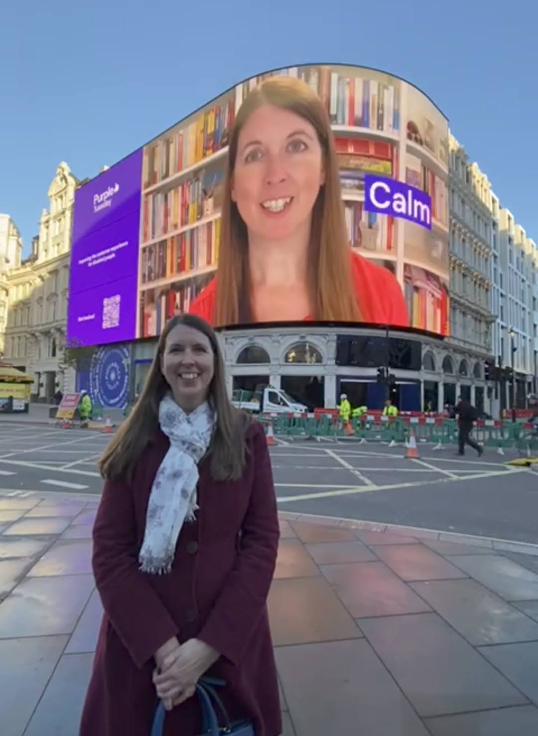 Photo of Sarah, a business mentor, in front of Piccadillly Circus where there is a video of her playing on the big screens