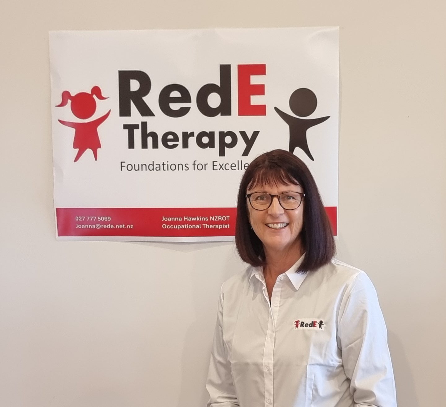Joanna Hawkins, paediatric occupational therapist, smiling in front of the RedE Therapy sign