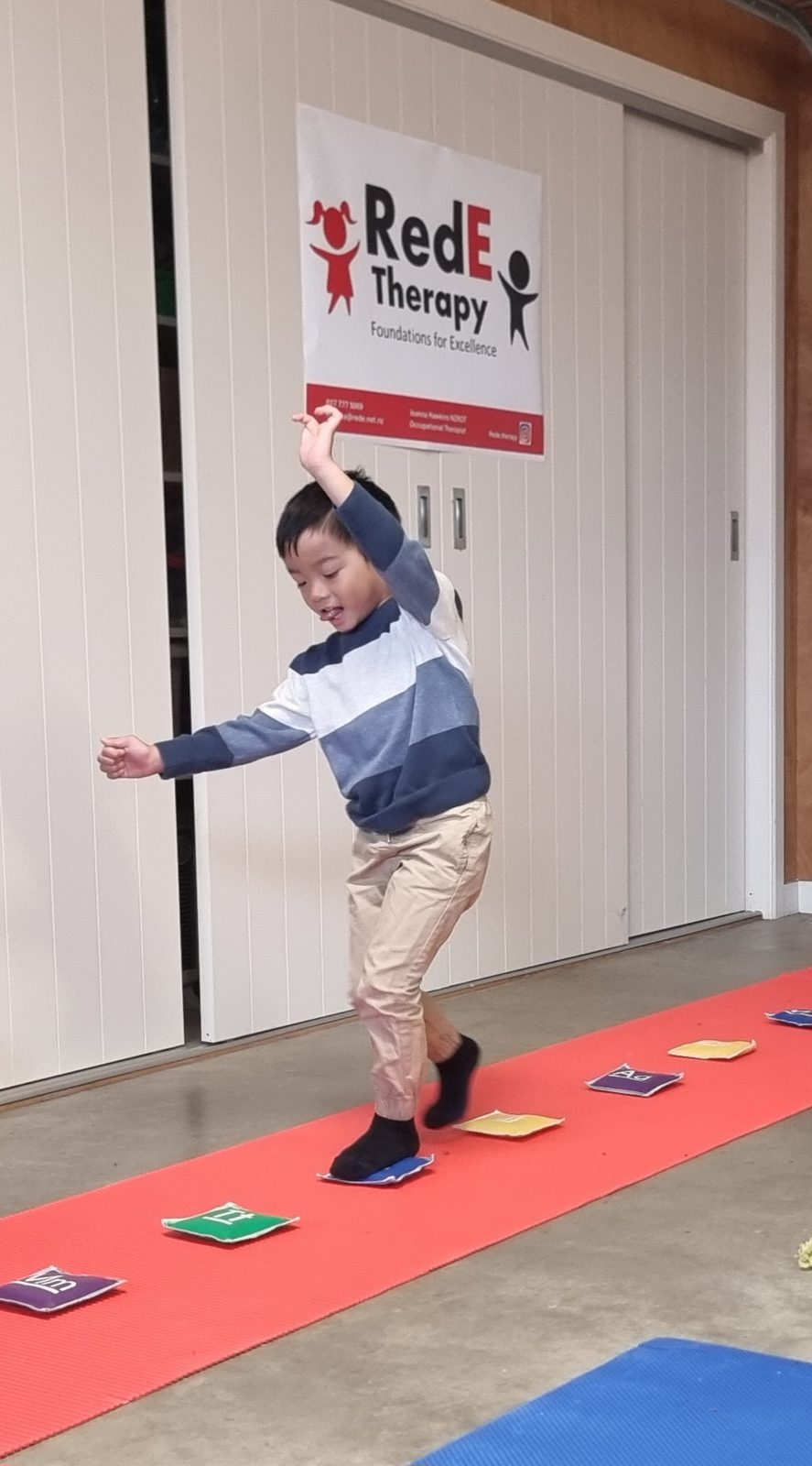 A child balancing and moving along a red mat with coloured beanbags at a RedE Therapy session