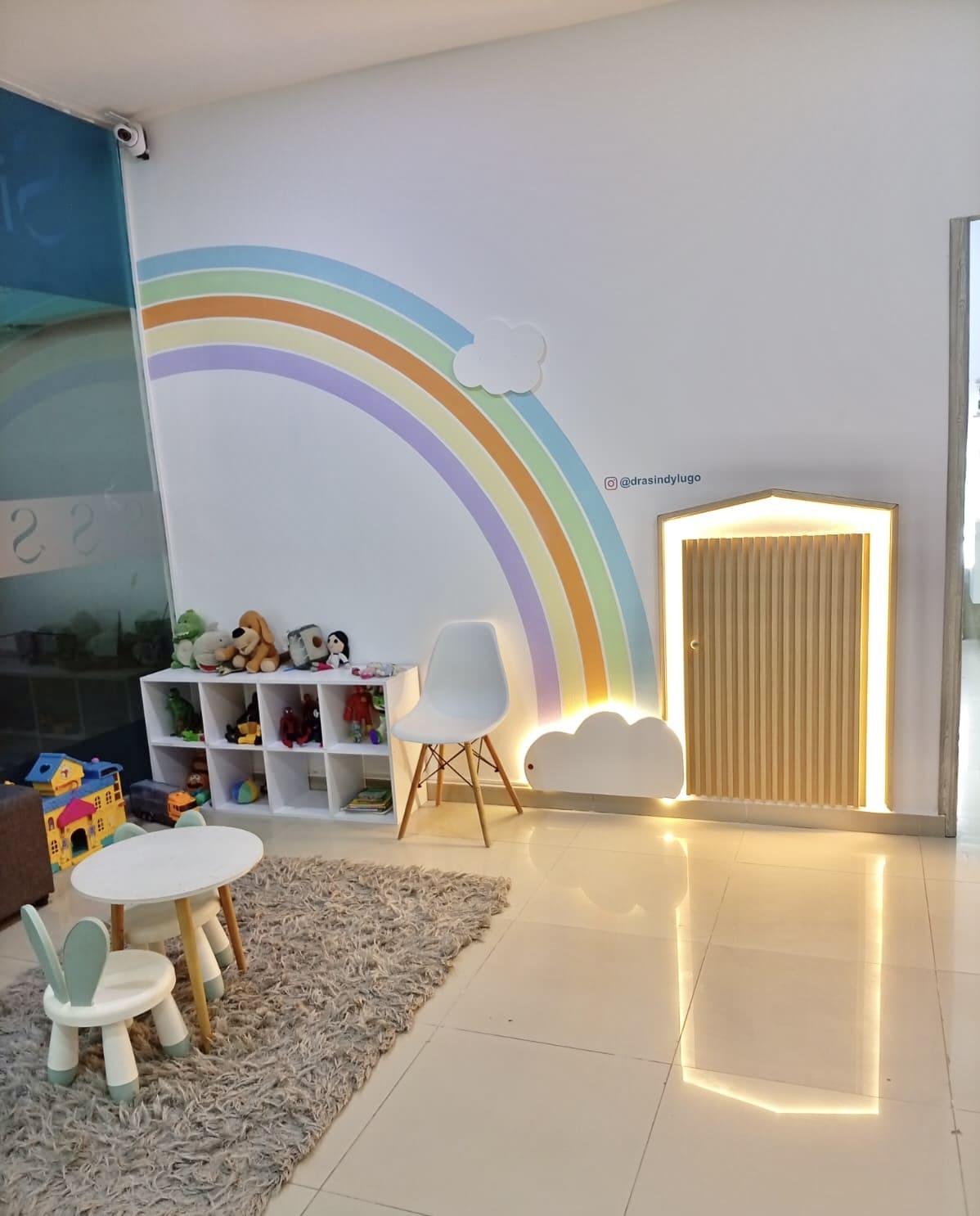 Sala de espera infantil con pared de arcoíris pastel, sillas en forma de conejo y estante de juguetes en el consultorio de Santa Marta