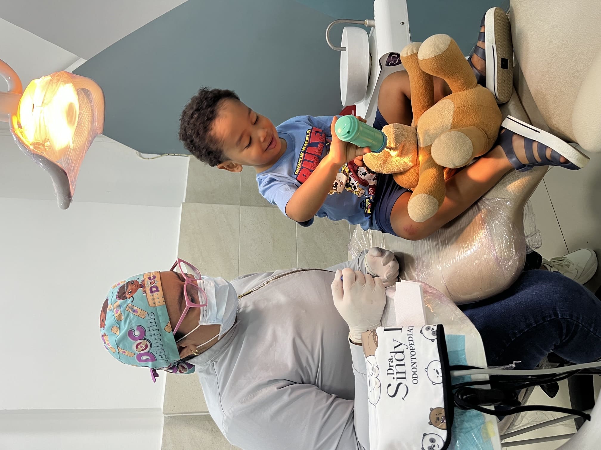 Odontopediatra con un niño pequeño que juega con un instrumento dental de juguete sobre un oso de peluche en Santa Marta