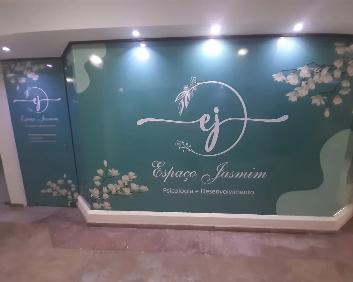 Entrada do Espaço Jasmim: parede verde com ramos de jasmim pintados e o logótipo