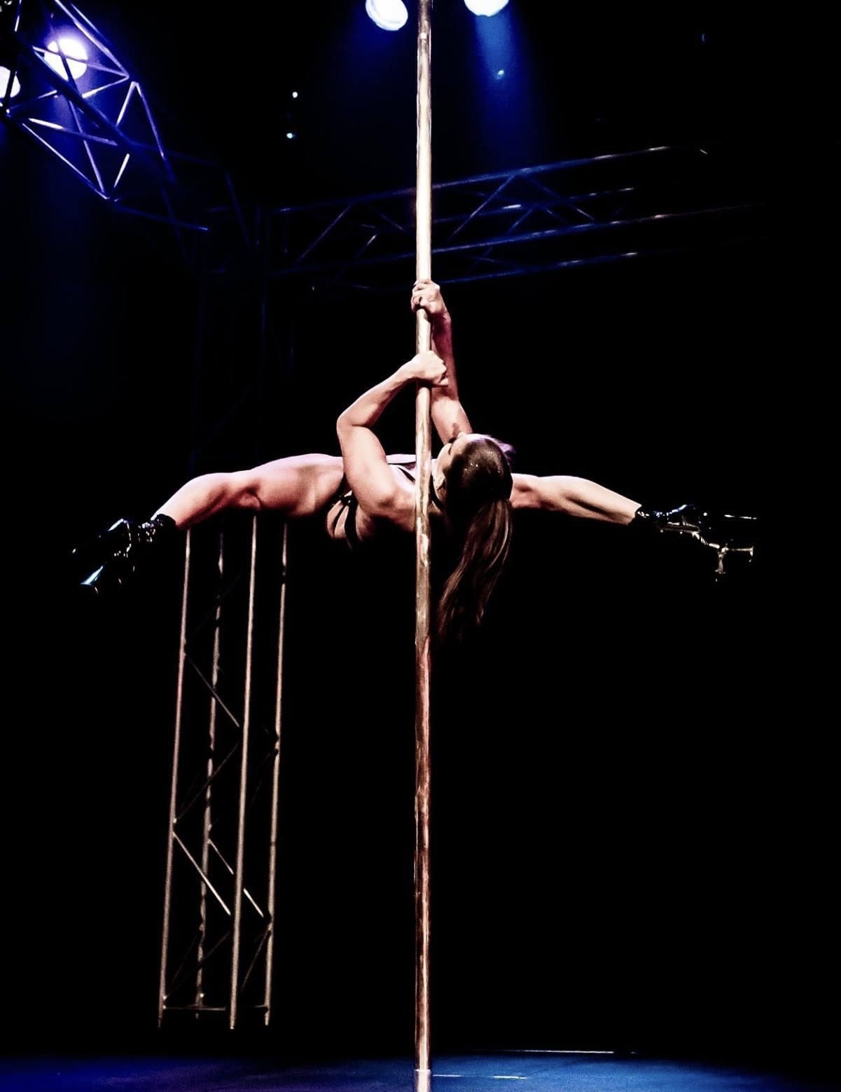 Andrea Ryff, two-time World Pole Champion, in a horizontal pole hold on a dark stage