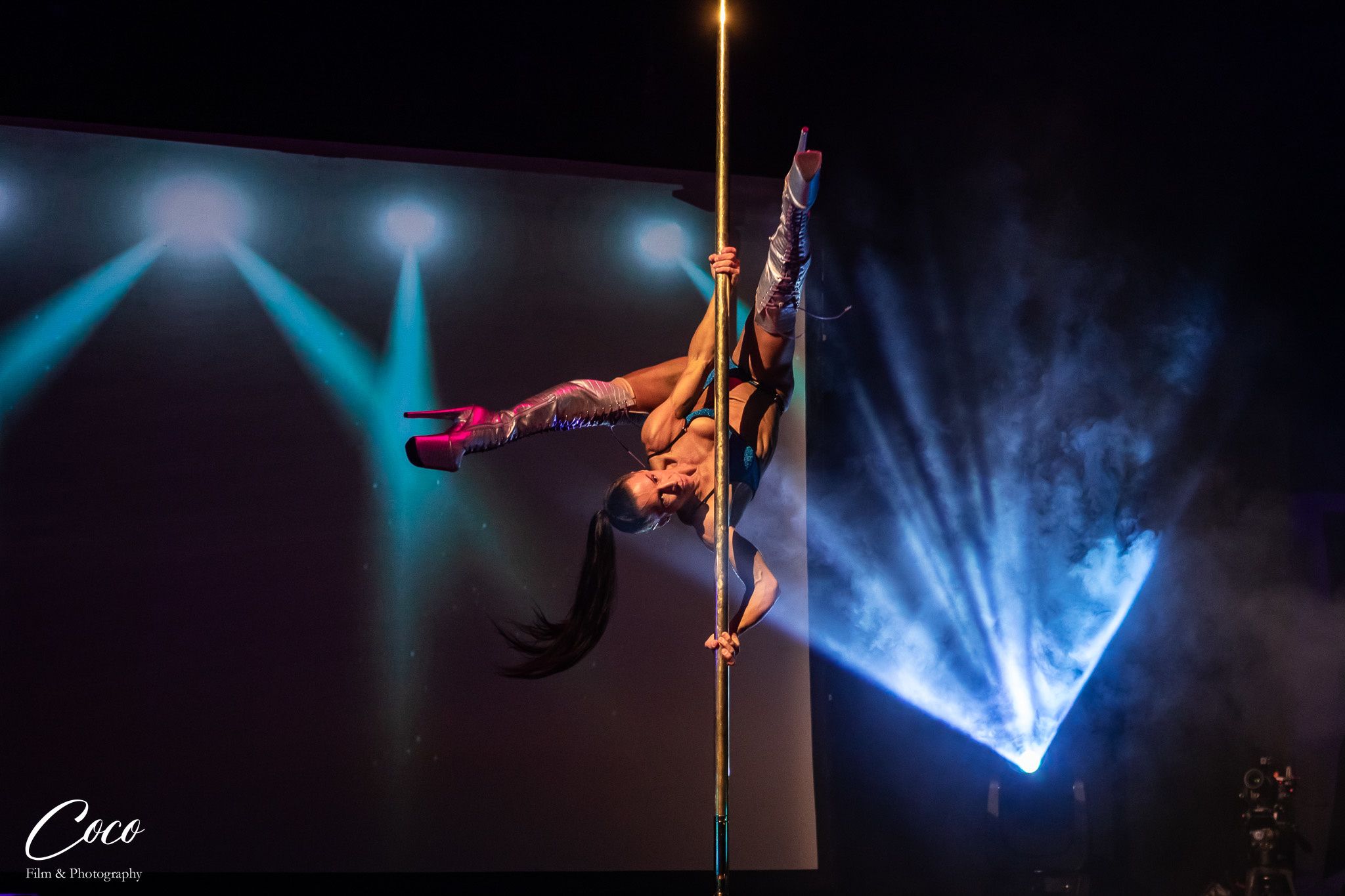 Natty Stephens inverted on the pole with blue stage lights