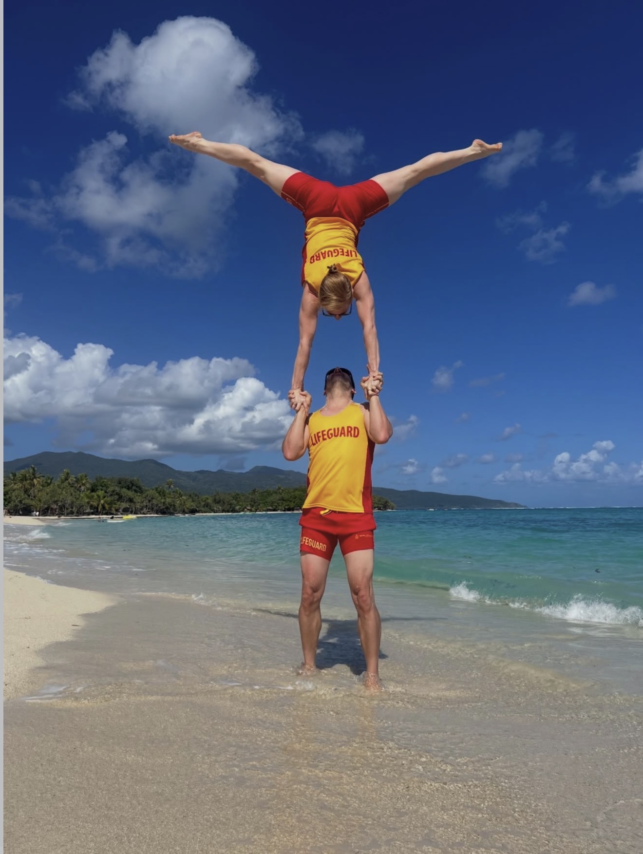 Toby J performing a partner acrobatic balance on a beach