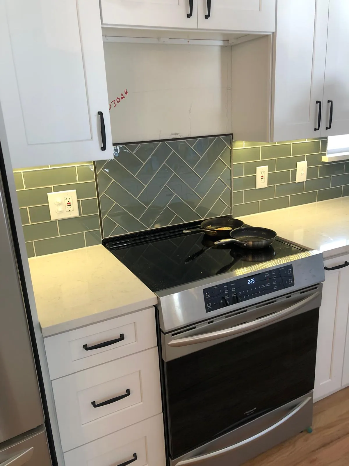 Kitchen range wall with green tile backsplash, under-cabinet lighting and slide-in range