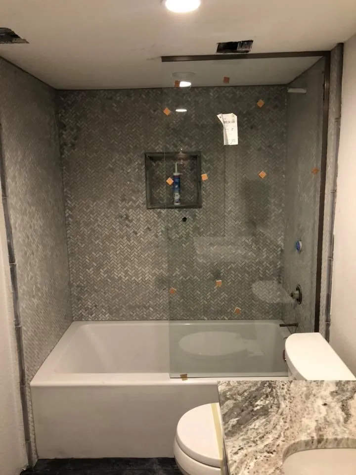 Bathroom remodel with tiled tub surround, glass panel and stone countertop