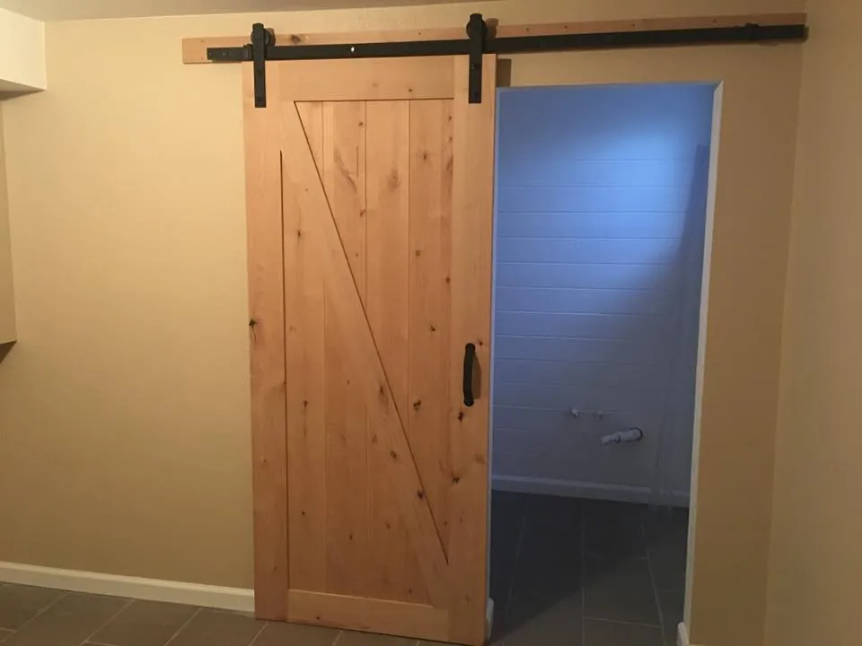 Sliding barn door in natural wood on a black rail beside a painted wall