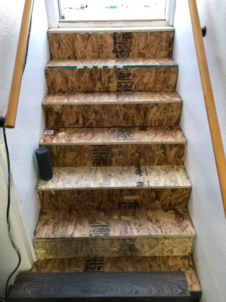 Staircase mid-remodel with stone-look treads and a wood handrail