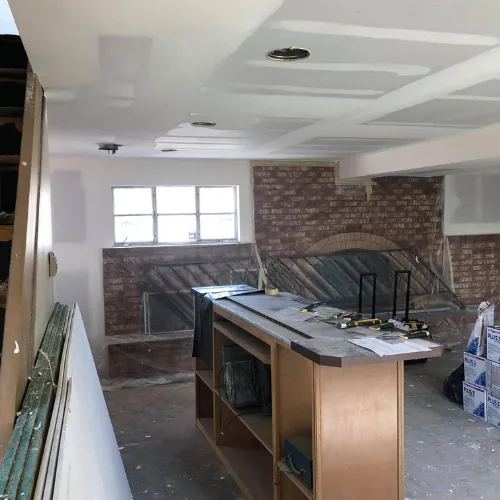 Interior renovation in progress with a brick fireplace and covered furnishings
