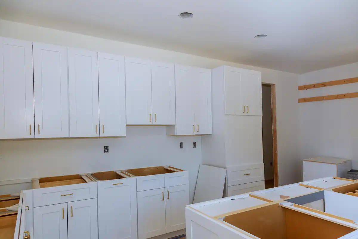White wall cabinets installed with base cabinet boxes staged on the floor below