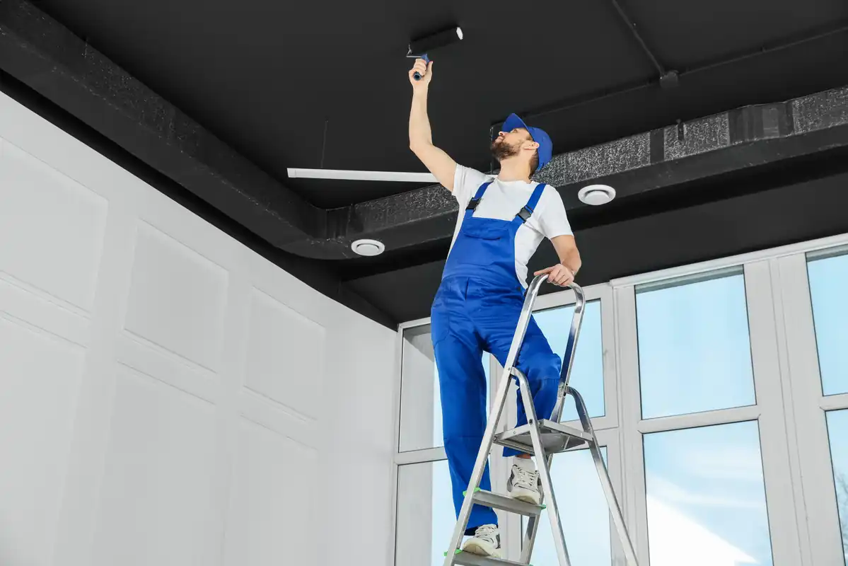 Painter on a ladder rolling a fresh coat across a high interior ceiling
