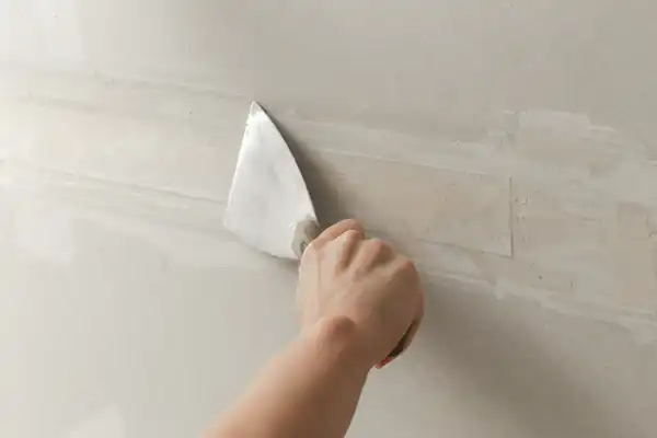 Taping knife drawing a thin coat of compound across a repaired wall section