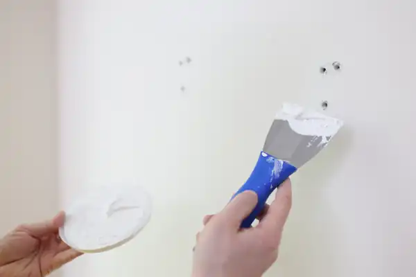 Small wall hole being filled with a putty knife before sanding and finishing