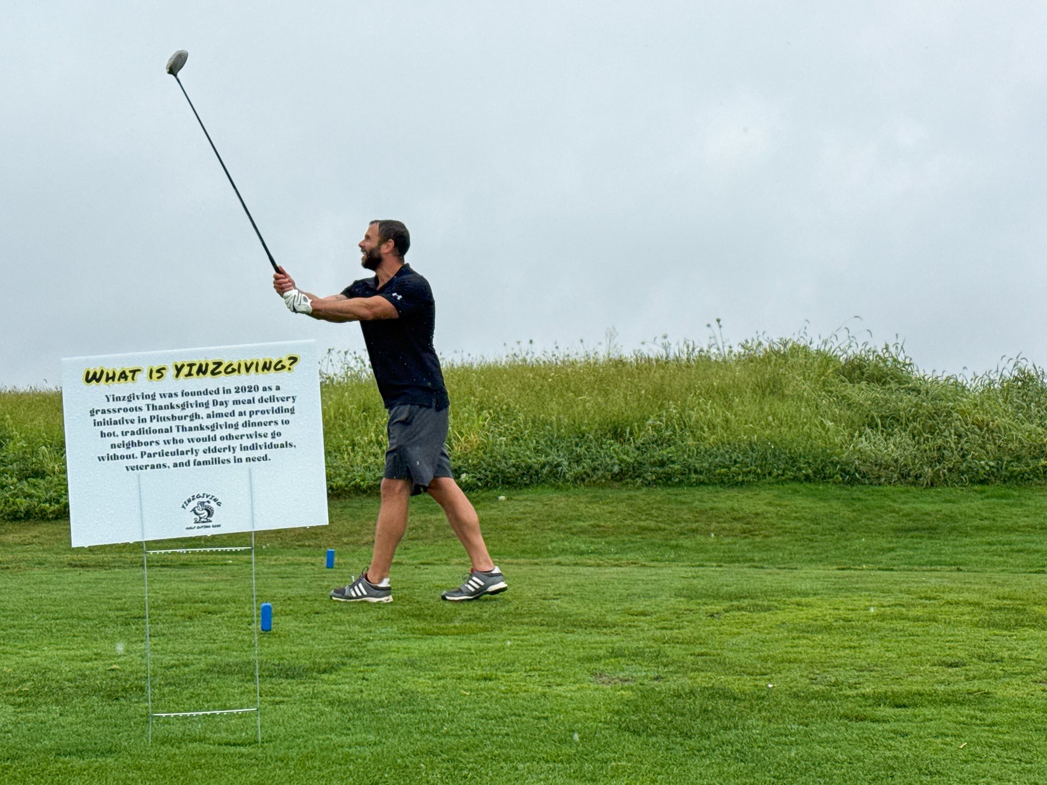 A golfer mid-swing with a What is YINZgiving sign in the foreground