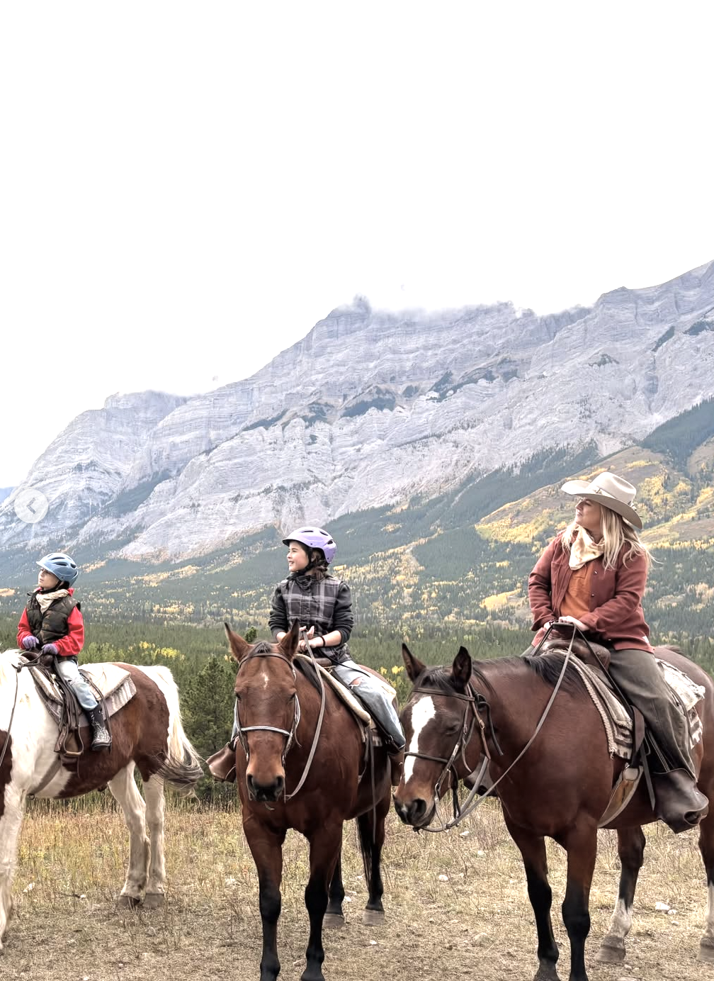 Horseback riders in custom hats in front of the Rocky Mountains