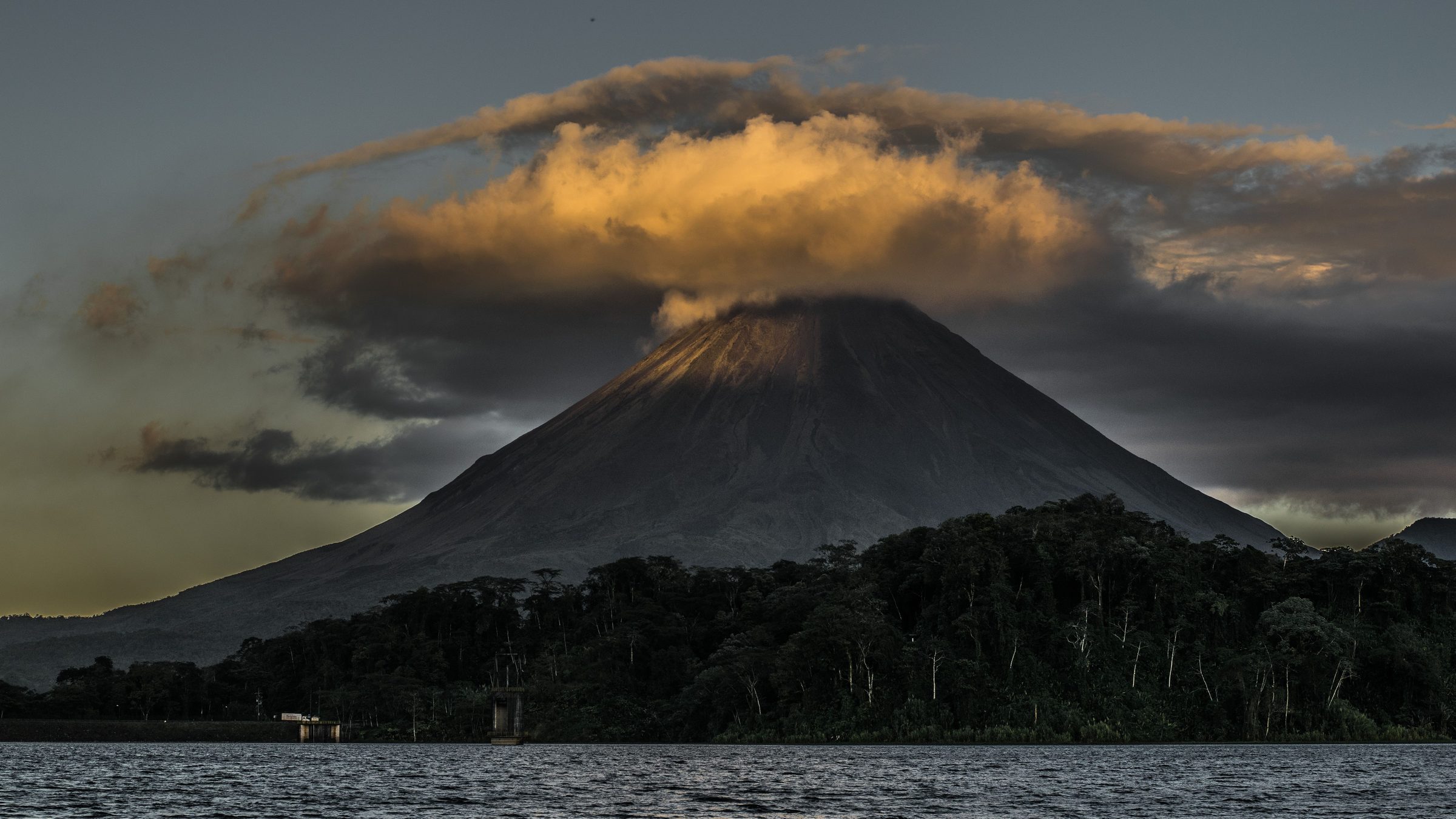Lake Arenal with Arenal volcano and a golden-lit cloud capping the summit