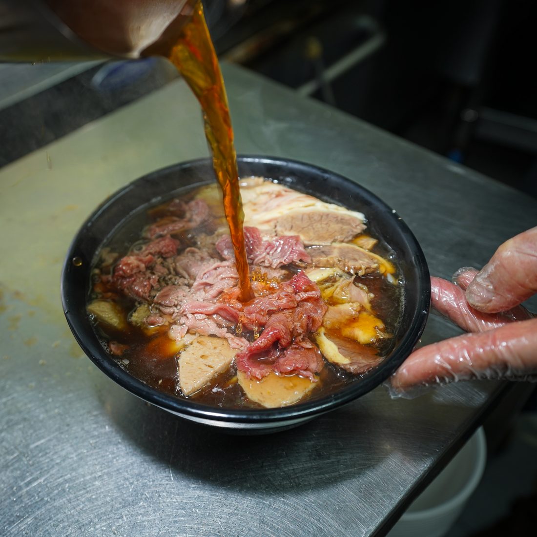 Twelve-hour beef broth being poured over rare beef and brisket for a House Special Pho